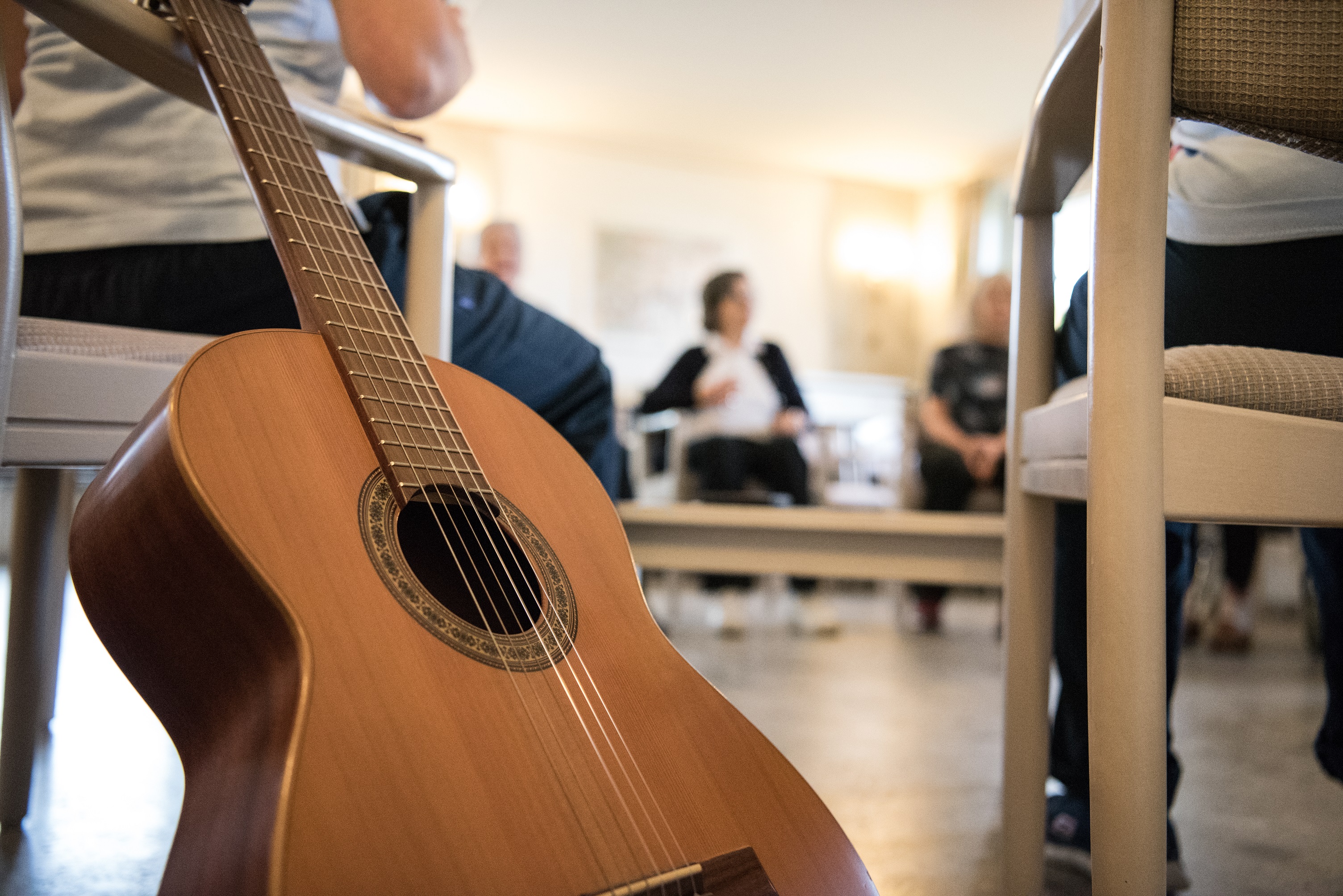 In einem Behandlungsraum befinden sich mehrere Patient*innen mit musikalischen Instrumenten, unter anderem einer Gitarre.